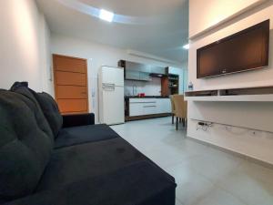 uma sala de estar com um sofá, uma televisão e uma cozinha em Apartamento novo , poucos metros da praia com WI FI em Ubatuba