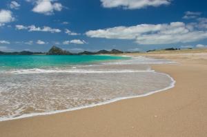 a sandy beach with the ocean and mountains in the background at Hiwi at Tahi - luxury bungalow with seaviews in Pataua