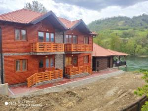 a wooden house with a large deck and water at Apartmani ODMOR NA DRINI in Ljubovija