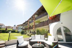 un patio con muebles blancos y una sombrilla verde en Aparthotel Kastel Seiser Alm, en Castelrotto