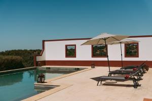 two lounge chairs and an umbrella next to a swimming pool at Herdade da Caniceira in Ervedal