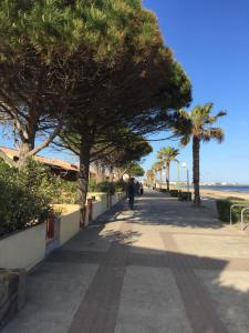 a person walking down a sidewalk next to the beach at New Maison tout confort, bord de mer avec Parking Privé in Gruissan