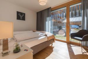 a bedroom with a bed and a chair and a window at Montela Hotel & Resort - Apartments in Saas-Grund
