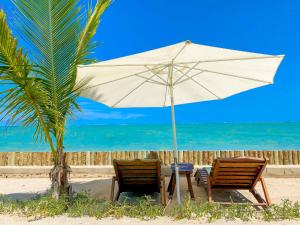 - une table et deux chaises sous un parasol sur la plage dans l'établissement Pousada Villa Tatuamunha, à Porto de Pedras