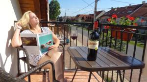 uma mulher sentada numa cadeira a ler um livro e uma garrafa de vinho em Gere Apartment de Luxe em Harkány