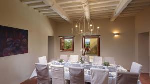 Habitación con una mesa larga con sillas blancas y una lámpara de araña. en CA MAGGIORE 10&2, Emma Villas en Castiglion Fibocchi
