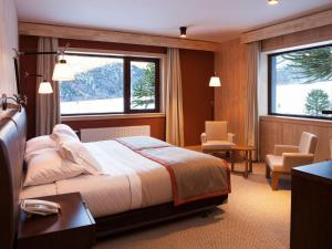 a bedroom with a bed and a desk and two windows at Valle Corralco Hotel & Spa in Malalcahuello