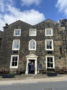 2 personnes debout à l'entrée d'un bâtiment en pierre dans l'établissement Talbot House Bed & Breakfast and Tearoom, à Pateley Bridge