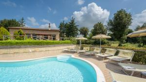 a pool with chairs and umbrellas and a house at L'Ovile 8, Emma Villas in Sovicille