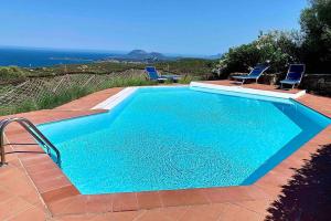 a large blue swimming pool with chairs and the ocean at Sunrise 14 in San Pantaleo
