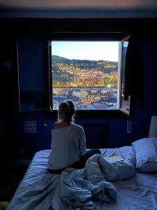 uma mulher sentada numa cama olhando pela janela em Superviews, parking 24h vigilado incluido y Netflix en habitación independiente con baño privado en apartamento particular, Français&English em Bilbao