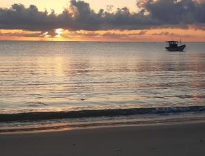 a boat in the ocean with a sunset in the background at Areia do Atlantico Hotel in Porto Seguro