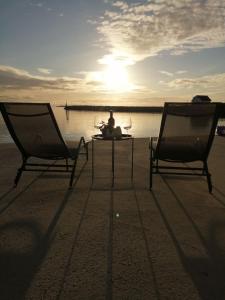 - deux chaises et une table sur la plage avec le coucher du soleil dans l'établissement Seaview apartment Karmøy, à Sæveland