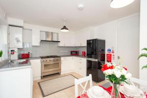 una cucina con armadietti bianchi e frigorifero nero di Stunning four bedroom house close to Excel, O2 & Central London with free parking a Londra