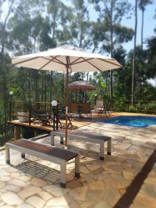 un patio con 2 bancos y una sombrilla junto a la piscina en Bendito Recanto en Penedo