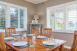 uma sala de jantar com uma mesa de madeira com cadeiras e janelas em Moruya Holiday House em Moruya