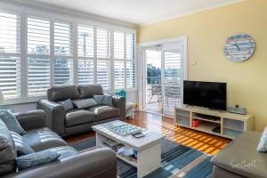 uma sala de estar com sofás e uma televisão de ecrã plano em Moruya Holiday House em Moruya
