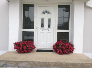 a white door with two geraniums in front of a house at Ardaobhainn in Letterkenny