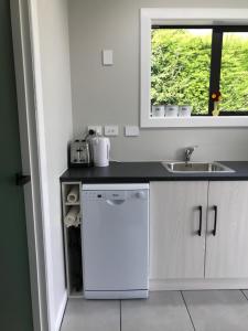 cocina blanca con fregadero y lavavajillas en Stump Cottage en Lumsden