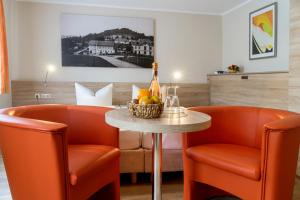 Pension Hotel Sartor في كورورت ألتنبرغ: غرفة مع كرسيين برتقال وطاولة مع زجاجة من الشمبانيا