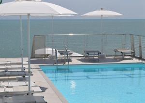 a swimming pool with chairs and umbrellas next to the ocean at Hotel Marco Polo in Caorle