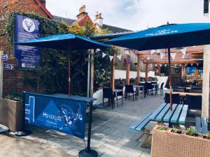 un patio con sombrillas azules, mesas y sillas en The Drymen Inn, en Drymen