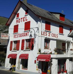ein großes weißes Hotel mit roten Rollläden auf einer Straße in der Unterkunft Hôtel les Deux Cols in Sainte-Marie-de-Campan