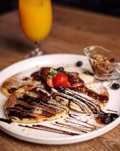 a plate of pancakes with berries and a glass of orange juice at Conti Hotel & Restaurant in Gjakove