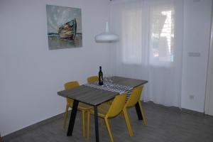 a dining room table with yellow chairs and a bottle of wine at SOLEIL - Newly renovated apartment close to the sea in Barbat na Rabu
