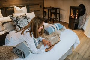 a woman laying on a bed reading a book at Cross Hill Glamping in Lake Hawea