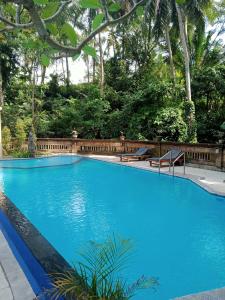 a large blue swimming pool with a fence and trees at Puri Bebengan Bungalows in Ubud