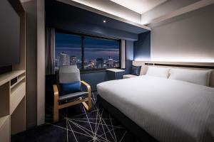 a hotel room with a bed and a chair and a window at remm plus Kobe Sannomiya in Kobe