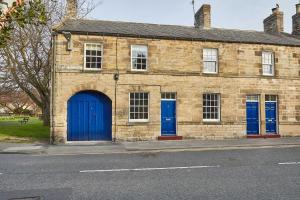 ein Backsteingebäude mit blauen Türen an einer Straße in der Unterkunft Host & Stay - The Blacksmiths in Warkworth
