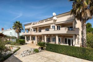 a large white building with palm trees in front of it at Apartmani Niko in Kožino