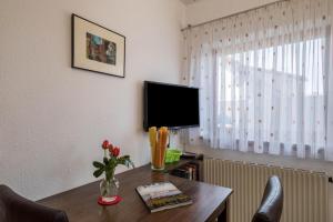 a room with a desk with a television and a table with flowers at Haus Schneider in Kressbronn am Bodensee