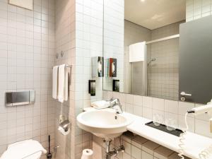 ein weißes Badezimmer mit einem Waschbecken und einem Spiegel in der Unterkunft Plaza Hotel & Living Frankfurt in Frankfurt am Main