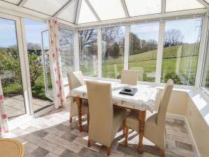 a conservatory dining room with a table and chairs and windows at Glan Y Gors Cottage in Llangerniew