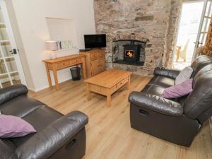 a living room with two leather couches and a fireplace at Glan Y Gors Cottage in Llangerniew