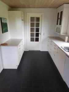 une cuisine avec des placards blancs et un sol noir dans l'établissement Elmely, à Dybvad