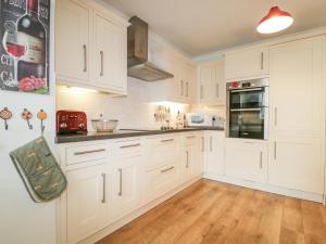 a white kitchen with white cabinets and wooden floors at Riverside Cottage in Cockermouth