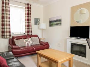 a living room with a red leather couch and a fireplace at Beech Tent Lane Cottage in Kelso