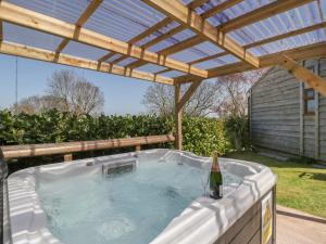 a hot tub under a wooden pergola with a bottle of wine at Cherry Lodge in Watchet