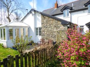 a cottage with a fence and flowers in front of it at Glan Y Gors Cottage in Llangerniew