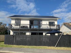a white house with a black fence and an umbrella at Sand Dunes Retreat in Otaki Beach