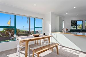 a kitchen with a wooden table and chairs and large windows at The Lights House - Beachfront Ohope Holiday Home in Ohope Beach