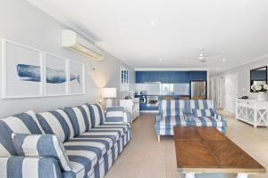 ein Wohnzimmer mit blau und weiß gestreiften Sofas und eine Küche in der Unterkunft Hamptons Meets Hervey Bay In Upmarket Resort - Ocean Views in Hervey Bay