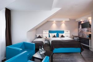 a hotel room with two beds and a blue chair at ibis Styles Cologne Airport in Troisdorf