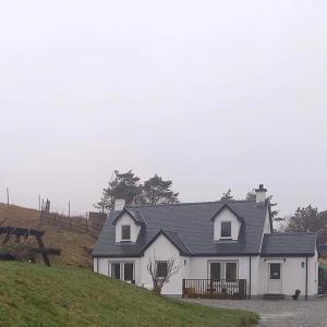 une maison blanche au sommet d'une colline herbeuse dans l'établissement Ard Na Mara Self Catering Isle of Mull, à Dervaig