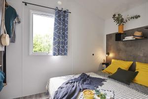 a bedroom with a bed with yellow pillows and a window at Camping Paradis le Rocher de la Granelle in Le Bugue +28 photos