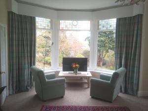 a living room with two chairs and a tv and windows at Strathview in Strathpeffer